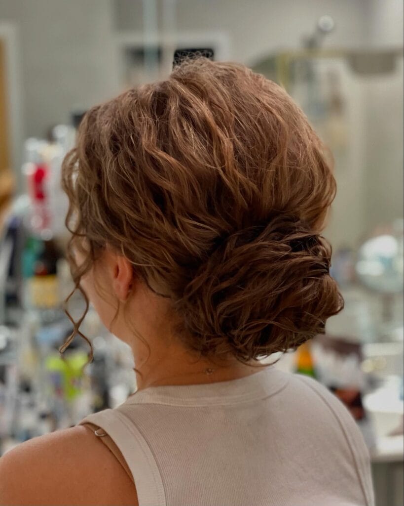Medium-length wavy light brown hair styled into a loose, messy chignon at the nape with soft tendrils left out for a relaxed, elegant look.