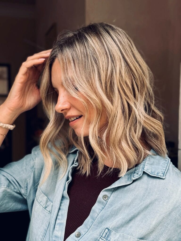 Shoulder-length blonde lob with soft layers, subtle highlights, and loose, natural waves parted slightly off-center for an effortless, textured look.