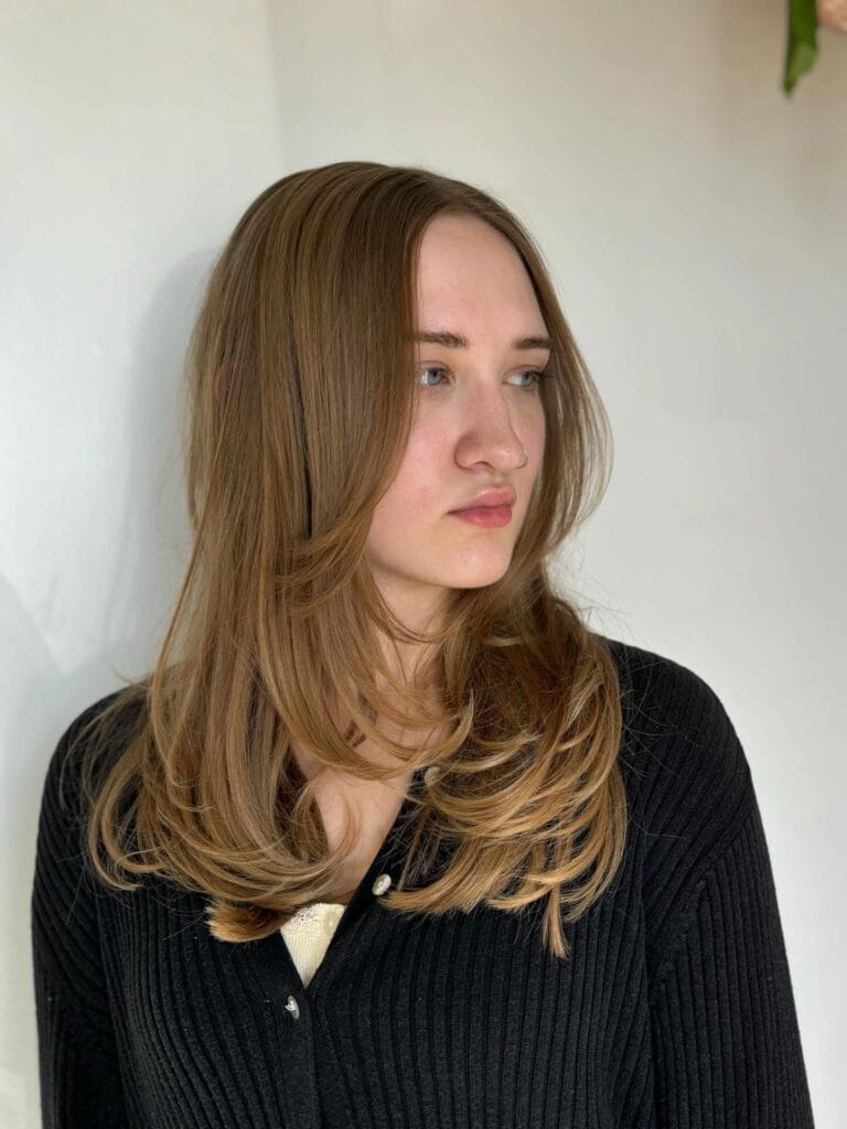 Medium-length light brown hair with soft internal layers and subtle face-framing pieces, styled smooth with slightly flipped-out ends for natural movement and volume.