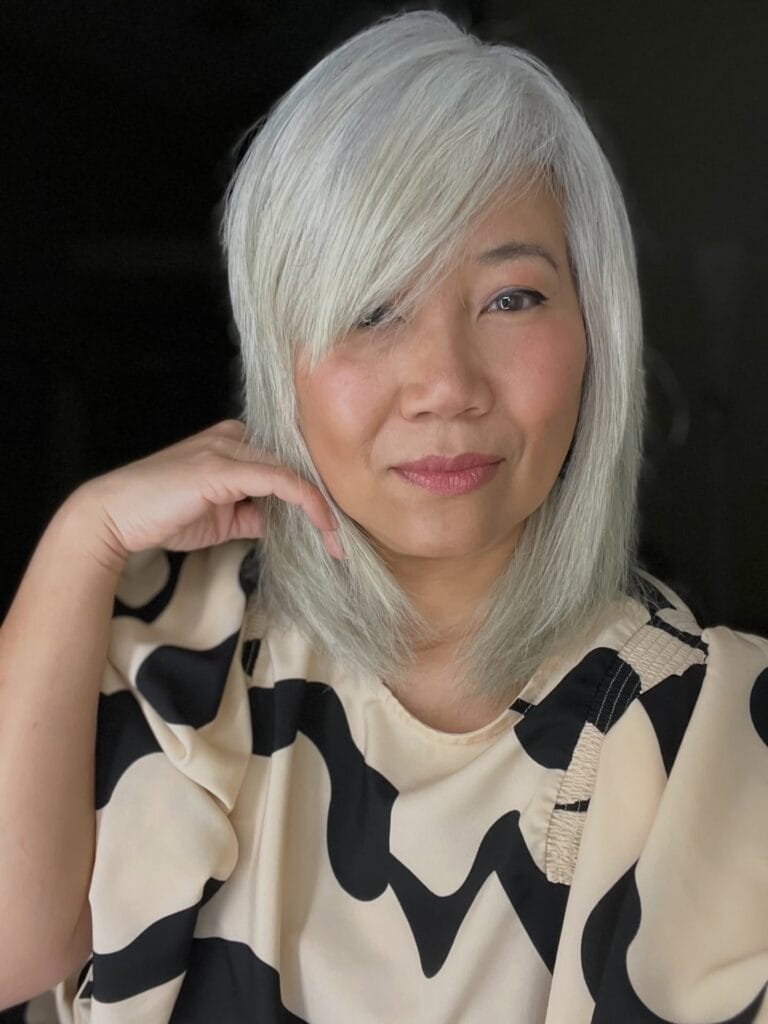 Mid-length straight silver hair with soft layers and long side-swept bangs that gently feather at the ends, creating a smooth, face-framing look.