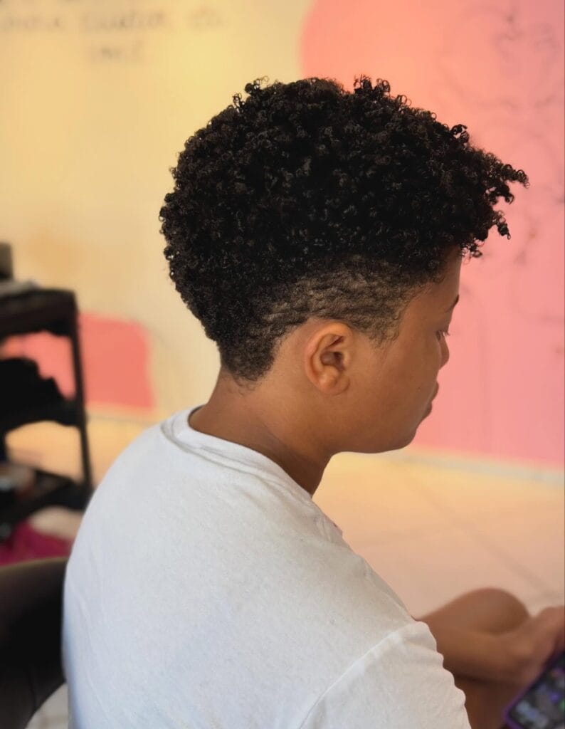 Short tapered haircut with tightly coiled natural curls on top and closely cropped sides and back for a clean, sculpted shape.