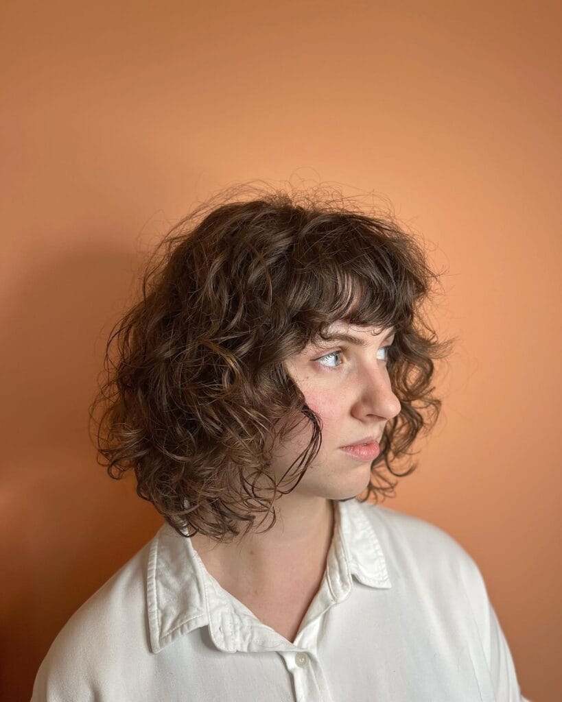 Short curly bob haircut with soft natural curls, chin-length layers, and wispy curly bangs framing the face.
