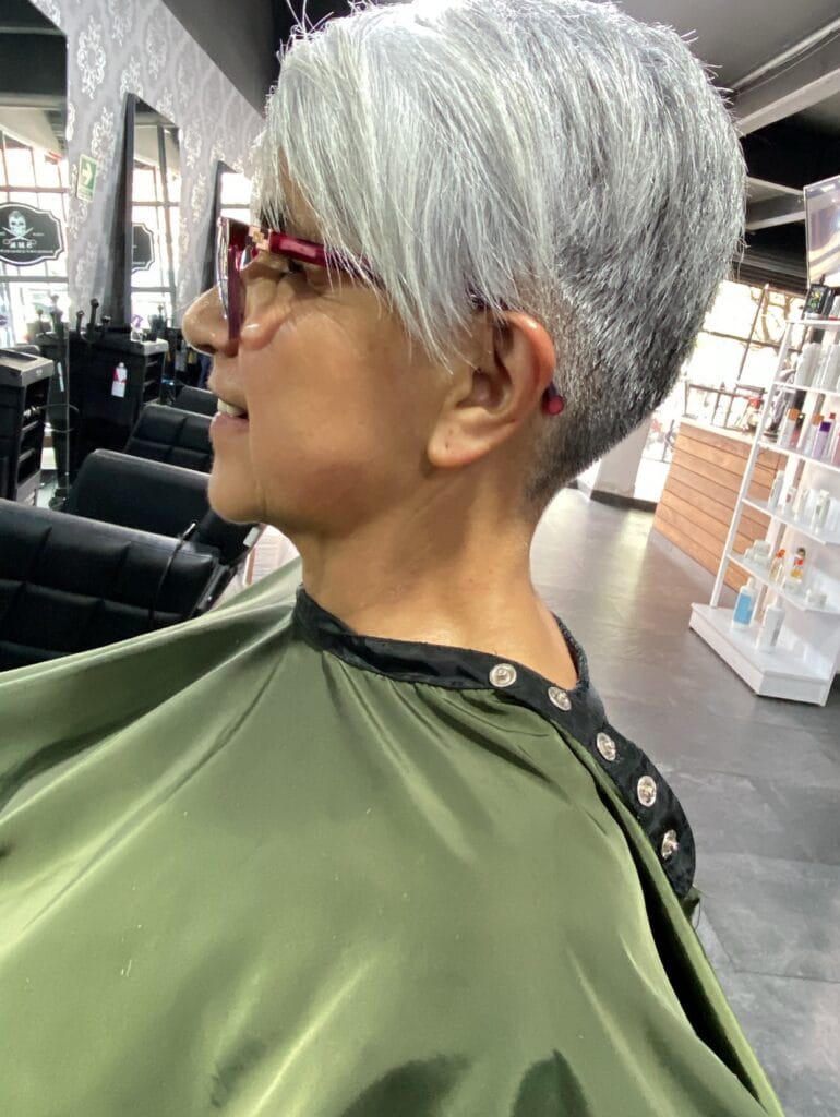 Short silver pixie haircut with tapered sides and back, longer layered top, and side-swept fringe for a clean, modern look.