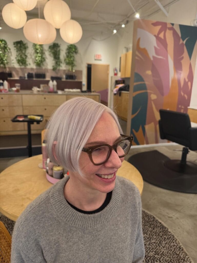 Short sleek pixie bob with icy platinum blonde color, softly side-parted with longer face-framing layers for a clean, modern look.
