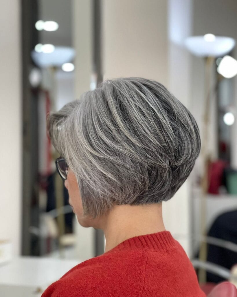Short layered silver pixie bob with softly stacked back and longer side-swept layers creating natural volume and movement.