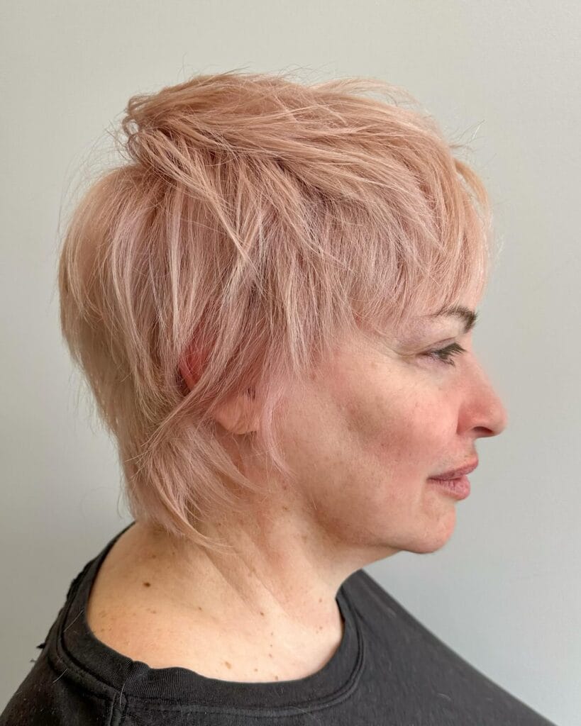 Short textured pixie haircut with choppy layers, soft volume on top, and wispy tapered pieces around the neckline in a light pastel pink shade.