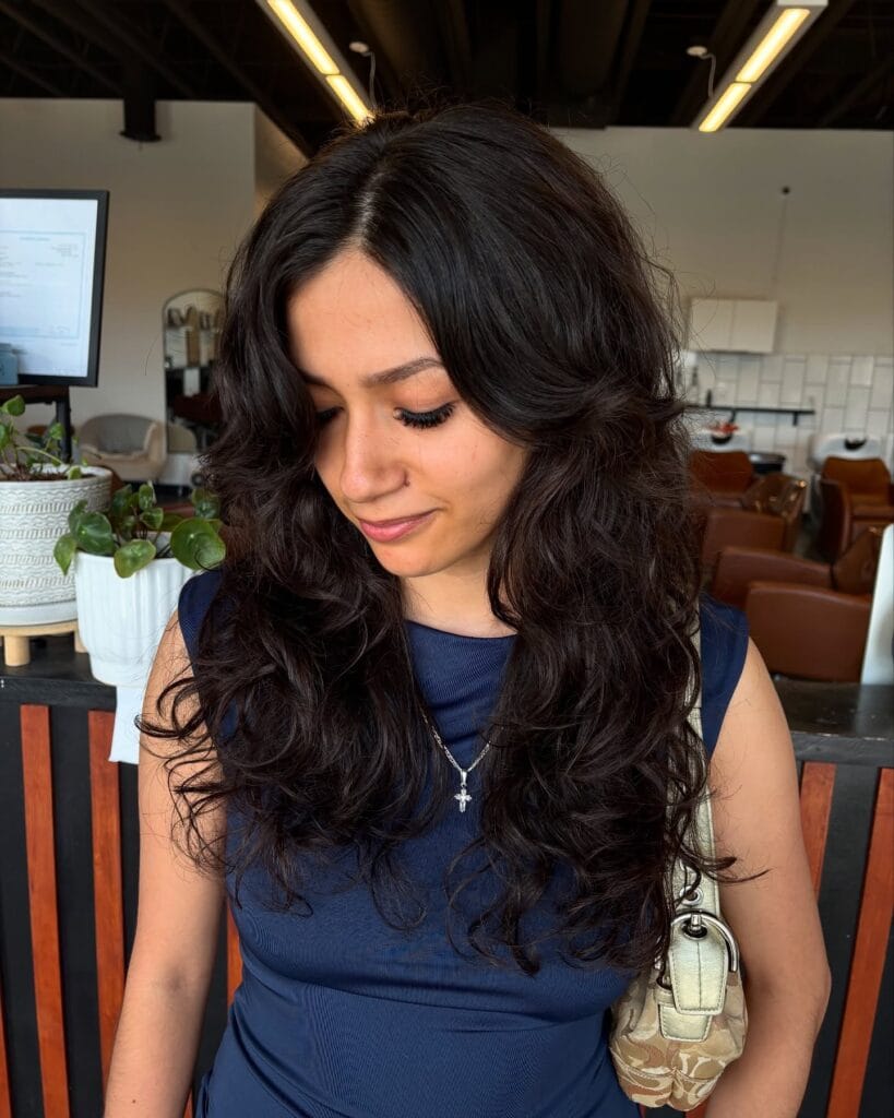 Shoulder-length dark brown hair styled with soft, voluminous curls and rounded layers, parted slightly off-center to frame the face naturally.