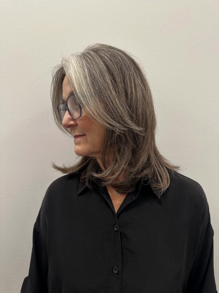Shoulder-length gray hair with soft face-framing layers and lightly feathered ends, styled smooth with gentle volume and a side part.