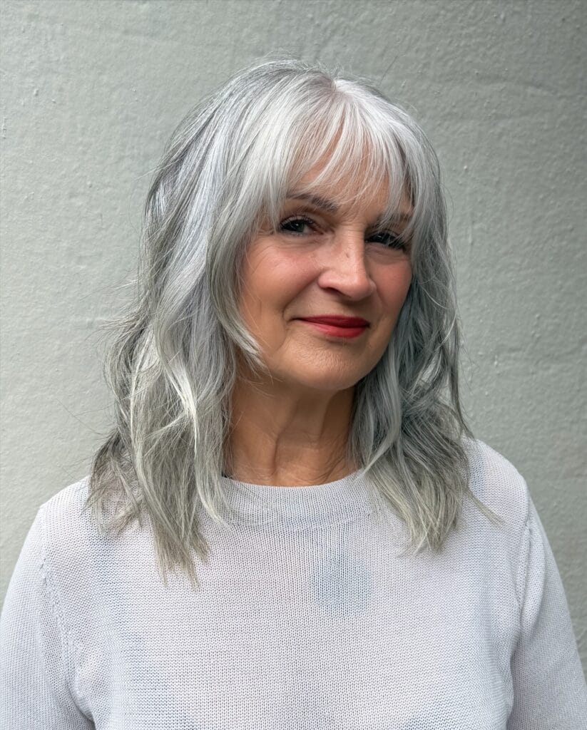 Shoulder-length layered silver hairstyle with soft texture and wispy bangs that gently frame the face.