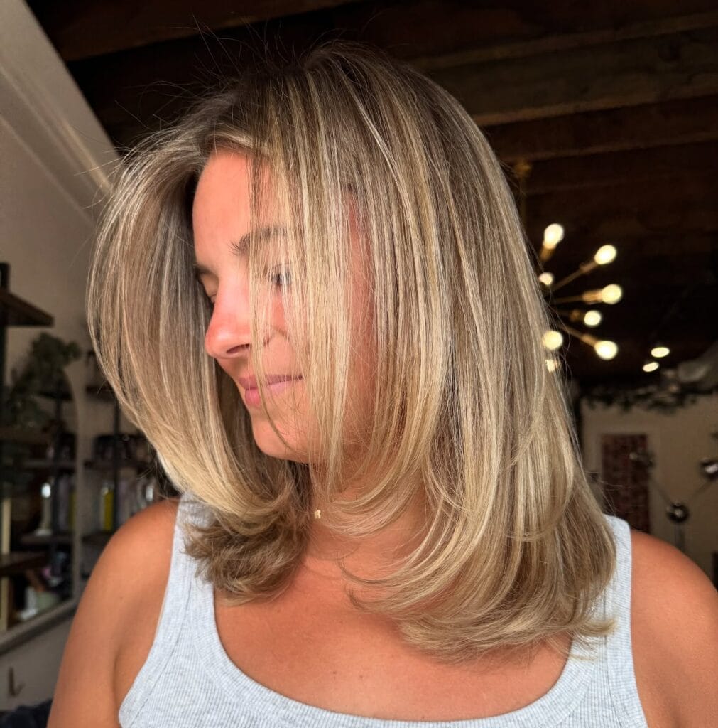 Shoulder-length layered blonde haircut with soft feathered ends and face-framing layers styled with volume and a subtle side part.