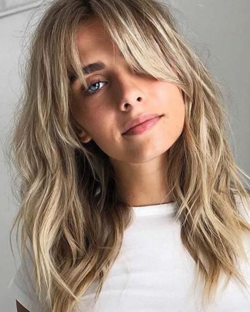 Shoulder-length blonde hairstyle with soft layered waves and airy curtain bangs that frame the face.