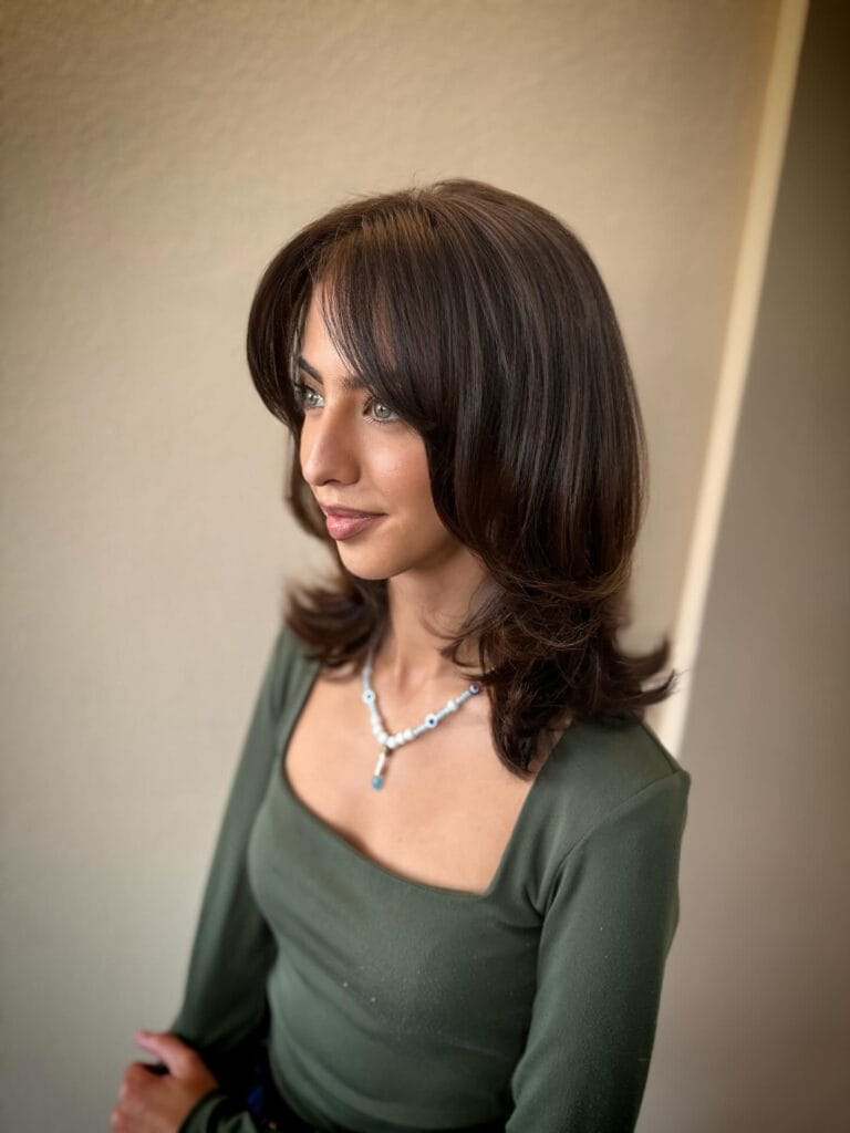 Shoulder-length layered haircut with soft feathered ends and subtle waves, styled with curtain bangs for a smooth, face-framing look.