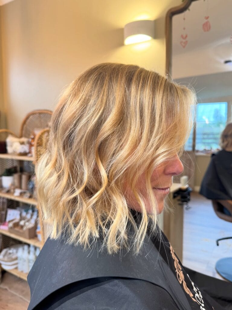 Shoulder-length layered lob with soft loose waves and blended blonde highlights for a textured, beachy look.