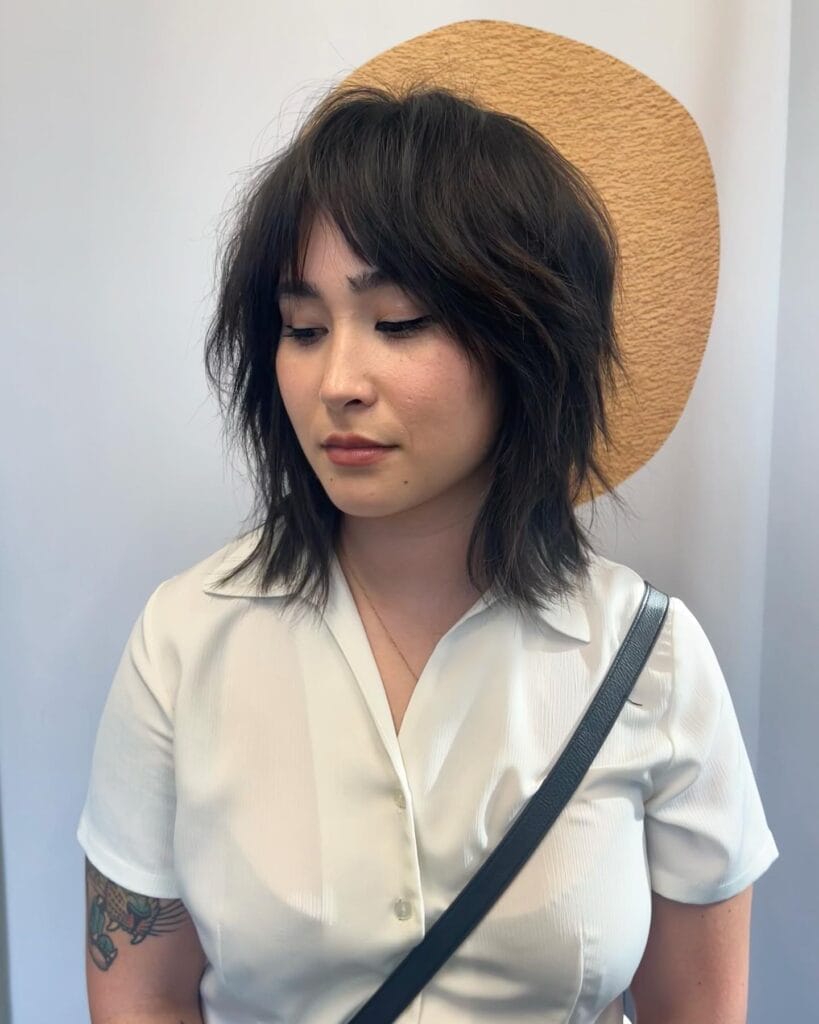 Shoulder-length shag haircut with soft choppy layers and wispy bangs, creating a textured, slightly tousled look.