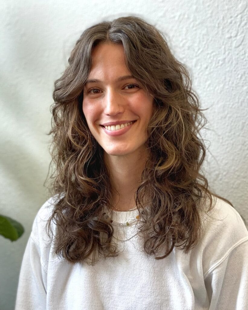 Shoulder-length wavy layered haircut with a soft center part, natural volume, and loose textured waves that frame the face for a relaxed, airy look.