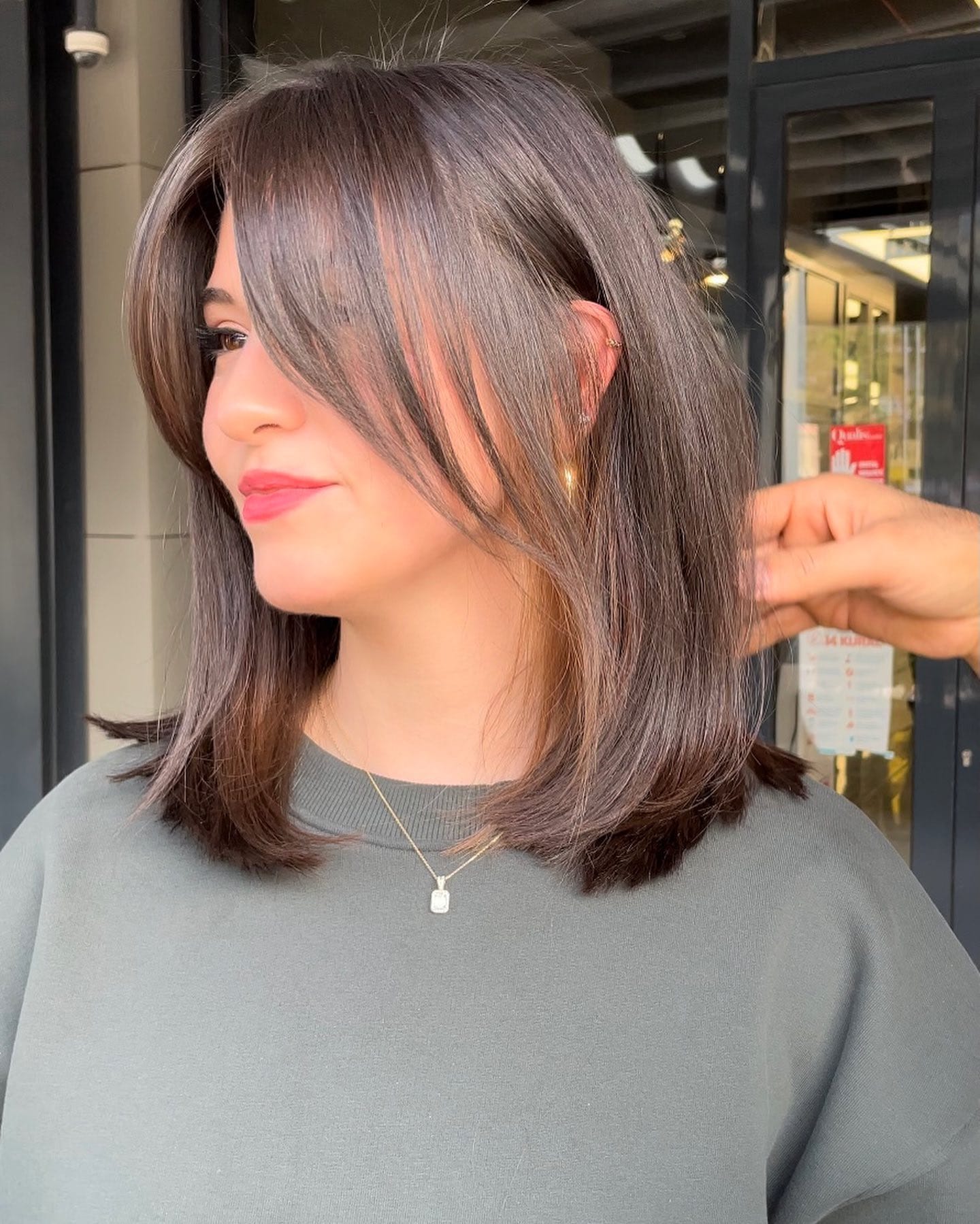 Shoulder-length layered bob with soft, smooth blowout styling and long side-swept bangs that frame the face.