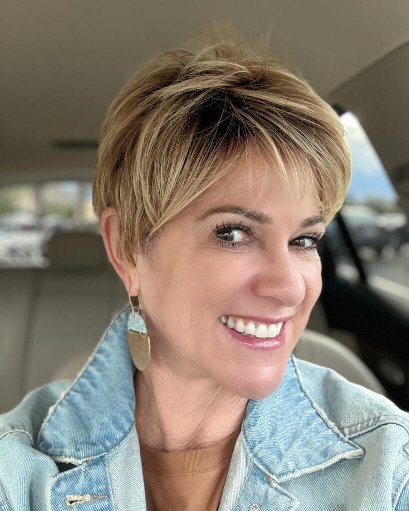 Short tapered pixie haircut with soft layers, side-swept bangs, and warm blonde highlights that add volume and dimension on top.