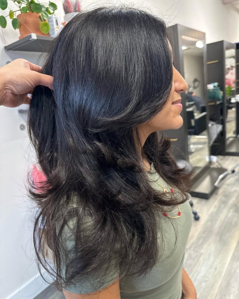 Long thick black wavy hair with glossy finish and face framing layers.