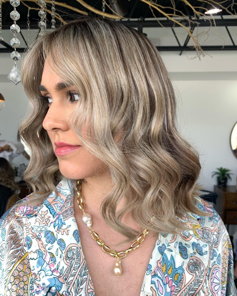 Shoulder length wavy lob with soft layers and cool toned blonde color with natural volume.