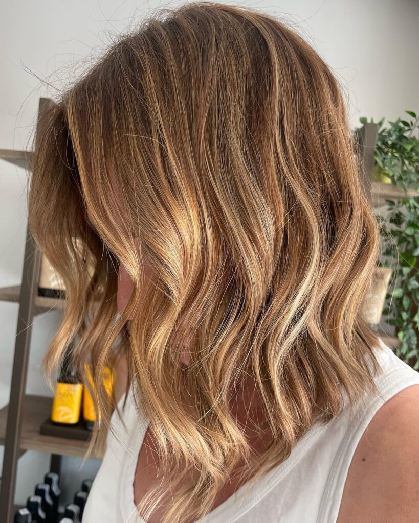 Wavy lob haircut with soft layers and warm blonde highlights for added dimension.