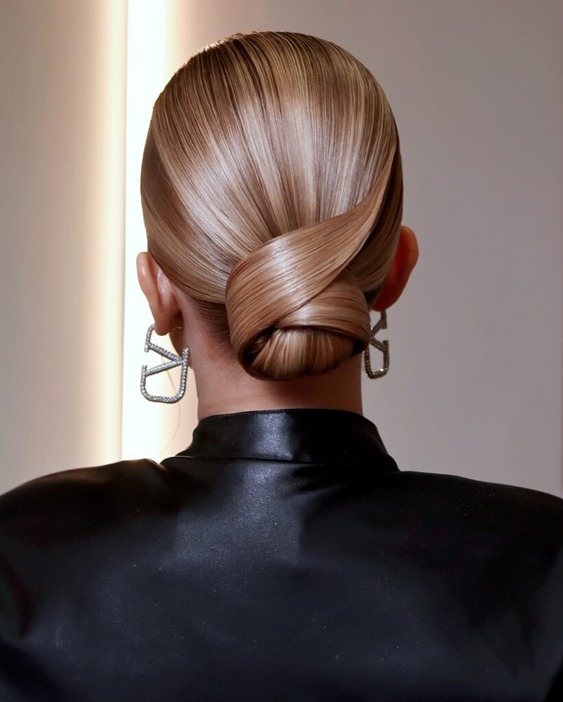 Sleek chignon with a glossy finish and tightly knotted structure at the nape.