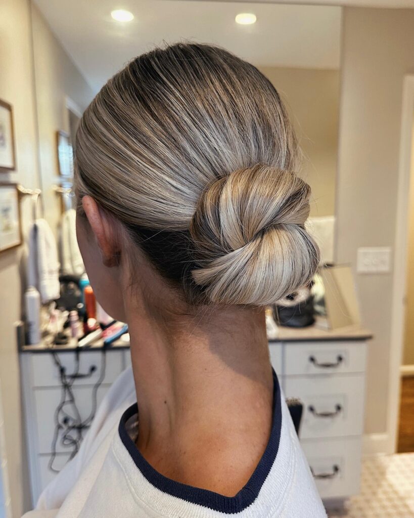 Blonde hair styled in a soft twisted low bun with smooth finish and subtle dimension.