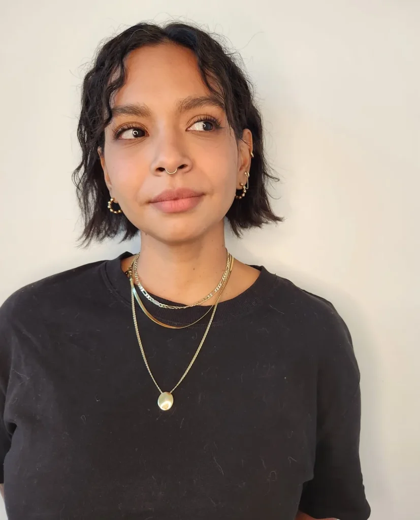 A woman with a textured chin length black bob and soft face framing waves looks off to the side.