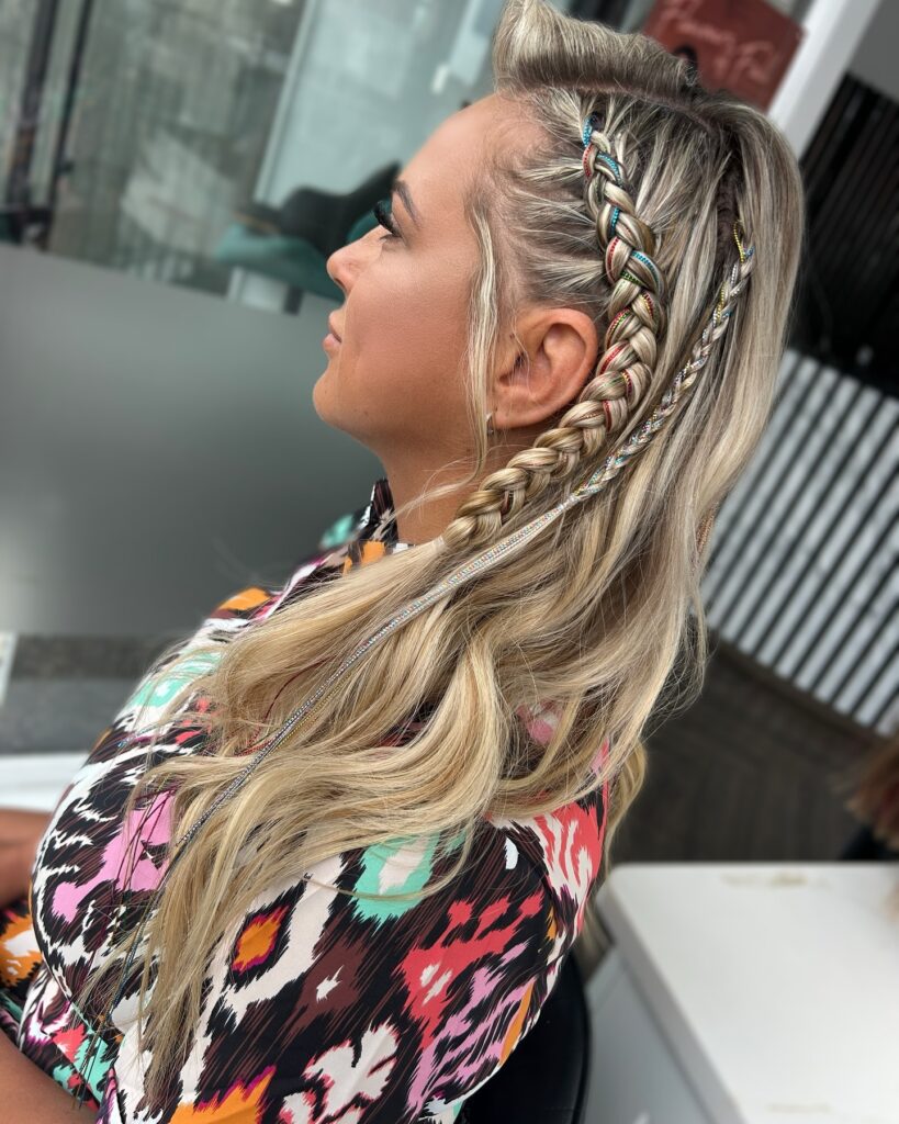 A woman with long wavy blonde hair featuring a side Dutch braid decorated with colorful sparkling rhinestones.