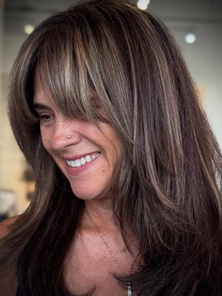 Long layered brunette hair with feathered curtain bangs blending into soft layers.