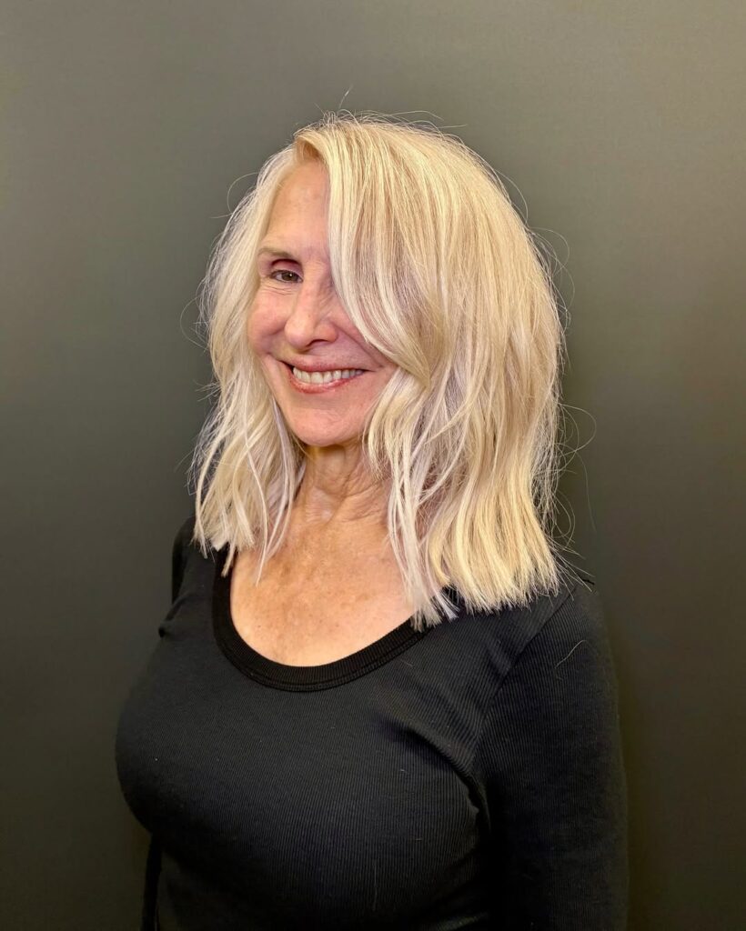 Long blonde wavy hair with soft side swept bangs blending into layers.