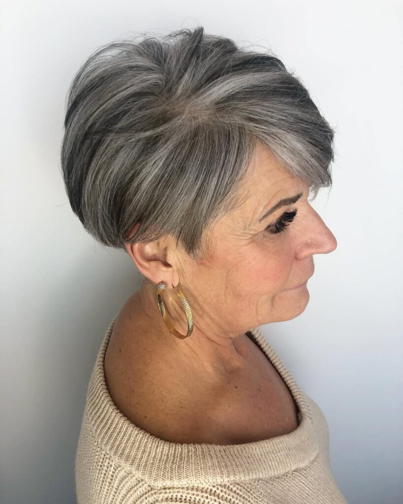 Short layered crop with volume and soft side swept bangs in salt and pepper tones.