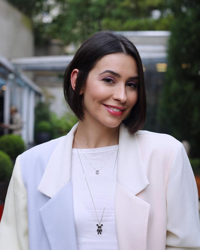 A smiling woman with a sleek middle parted dark brunette bob that is tucked behind one ear.