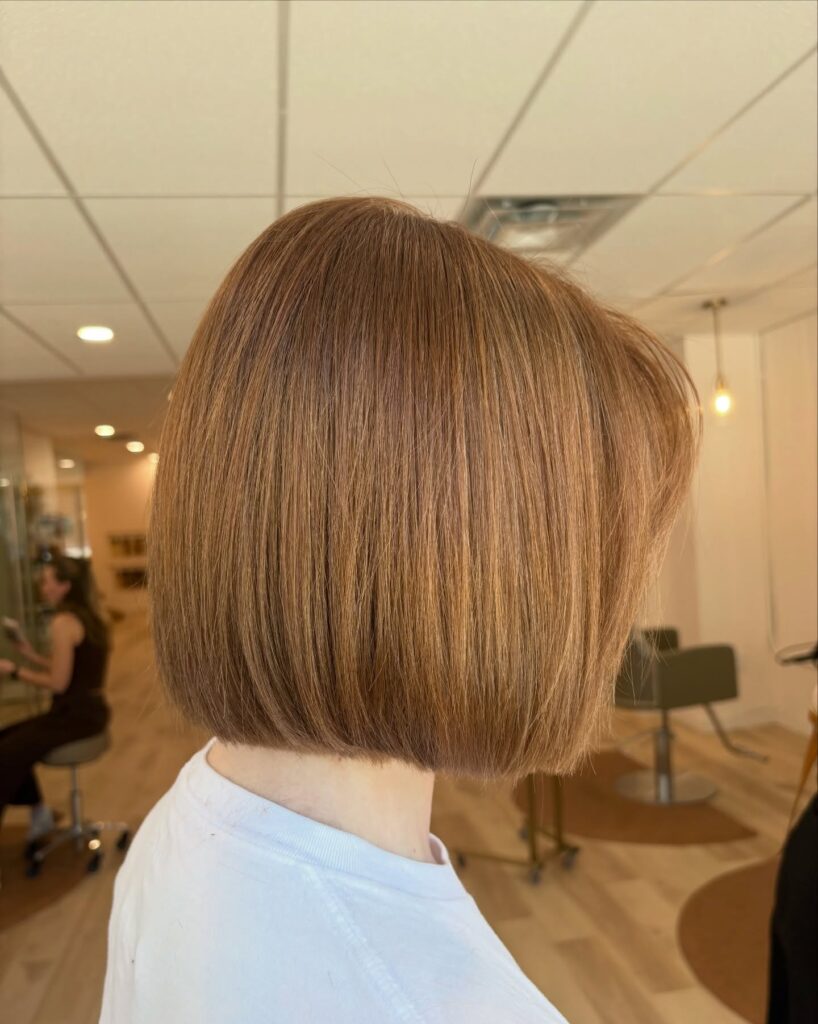 A side profile view of a woman with a sleek strawberry blonde bob cut in a sharp blunt line at the chin.