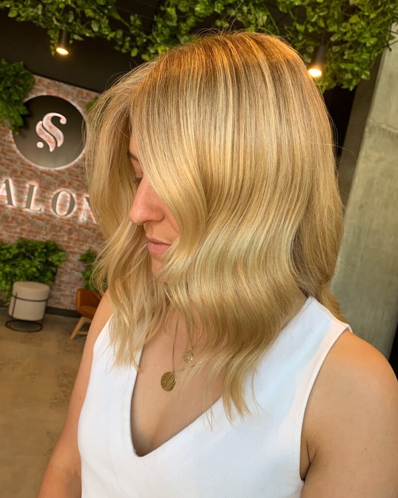 A woman with a honey blonde long bob styled in loose soft waves that reach her collarbone.