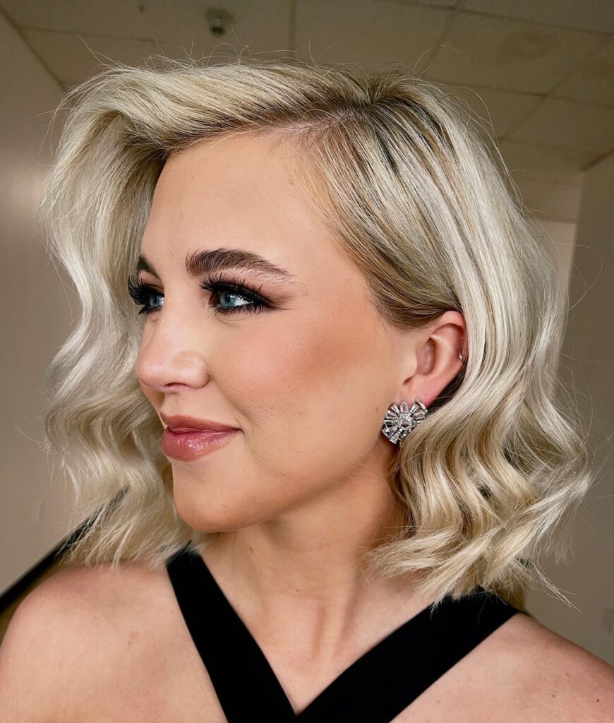 A woman with a platinum blonde short bob styled in elegant polished waves and tucked behind one ear.