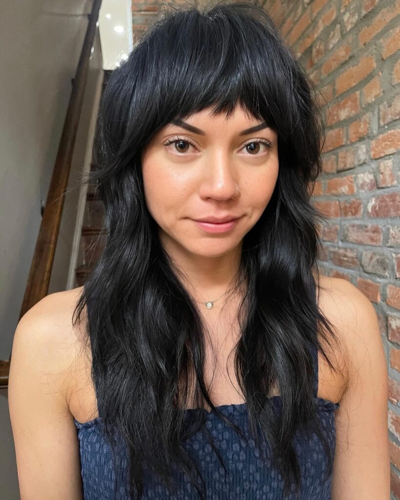 Long layered dark hair with soft bangs and textured shaggy ends.