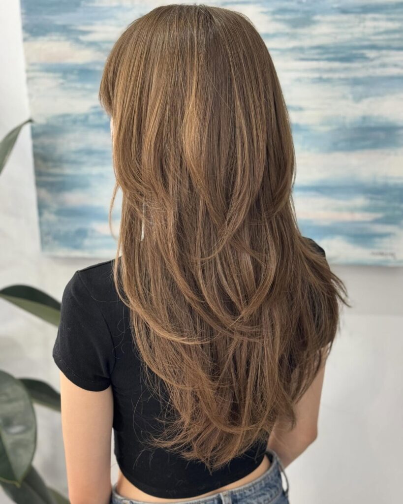 Long layered brown hair with soft waves and natural movement.