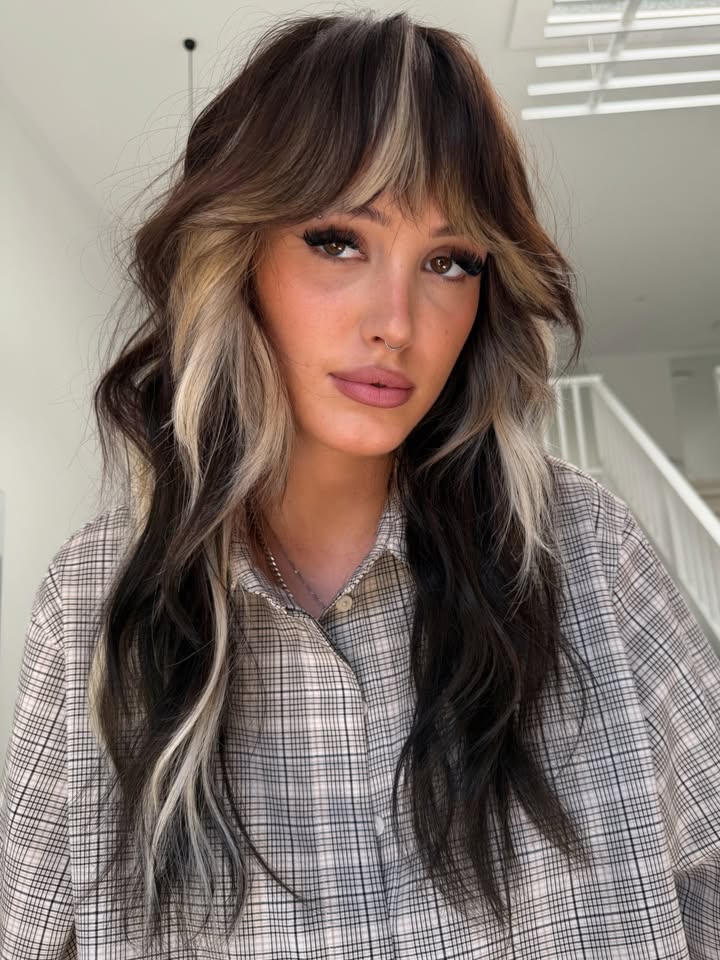 Medium length dark hair with blonde highlights, layered texture, and soft parted bangs.