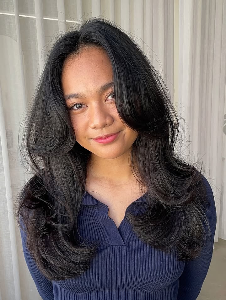 Medium length dark glossy hair with long layers and soft curtain bangs.