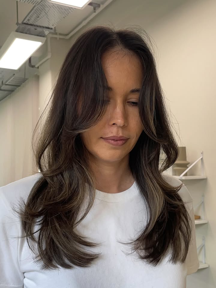 Medium length brunette hair with soft layers and curtain bangs styled with gentle curls.