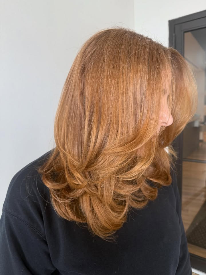 Medium length copper layered hair with soft blended bangs and bouncy ends.