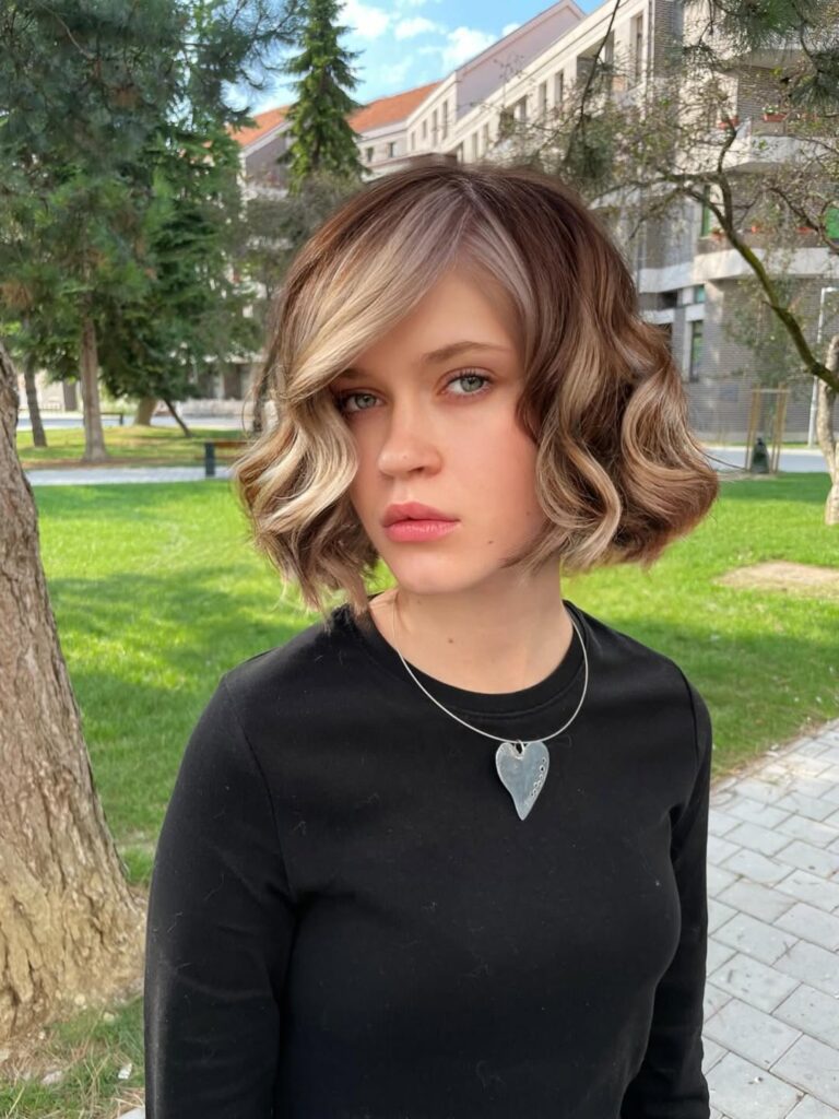 A woman with a sculpted wavy bob featuring soft face framing waves and blended highlights.