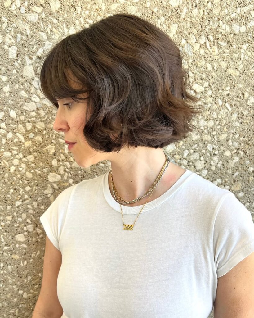 A woman with a short brunette wavy bob with a rounded shape and softly tucked ends.