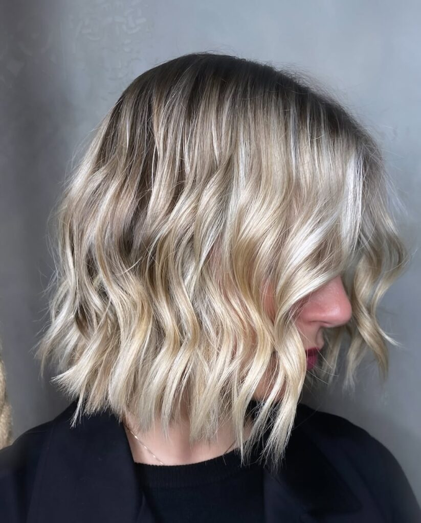 A woman with an icy blonde wavy bob with soft defined waves and darker roots.