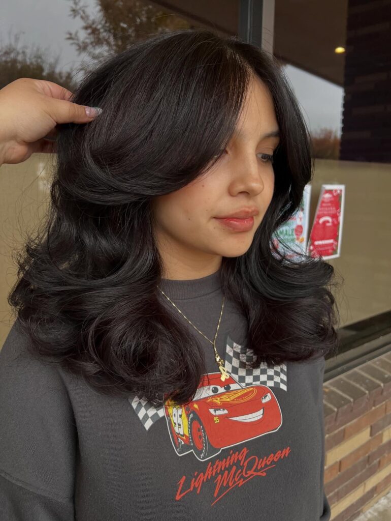 A woman with a mid length espresso brown butterfly haircut featuring dramatic face framing layers and bouncy curled ends.