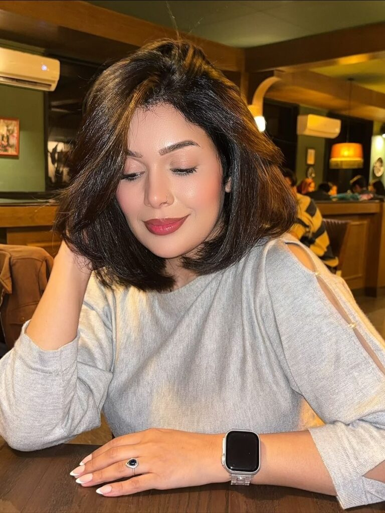 A woman with a voluminous brunette butterfly bob hairstyle featuring soft layers and a deep side part.