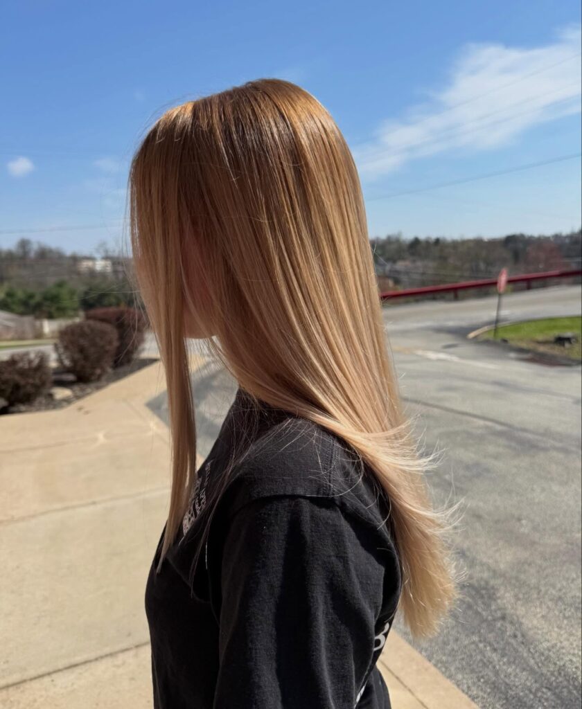 A woman with long straight strawberry blonde hair featuring warm copper highlights and soft feathered ends.