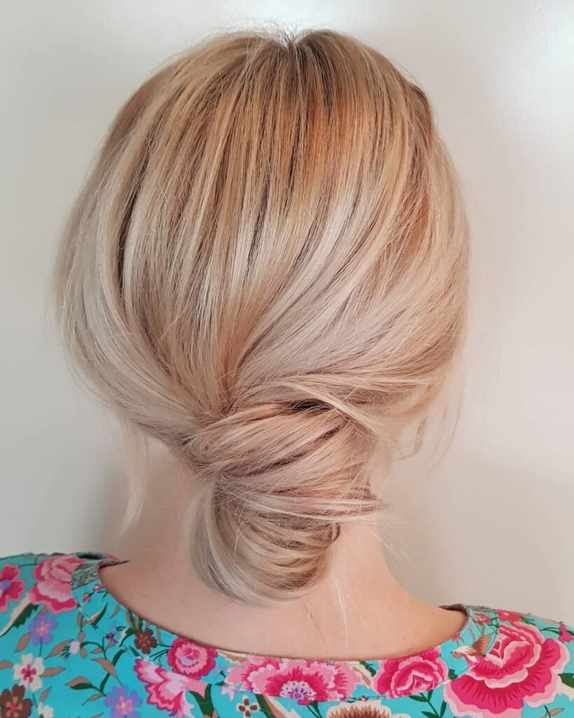 Blonde hair styled into a soft twisted low updo with a slightly textured finish.