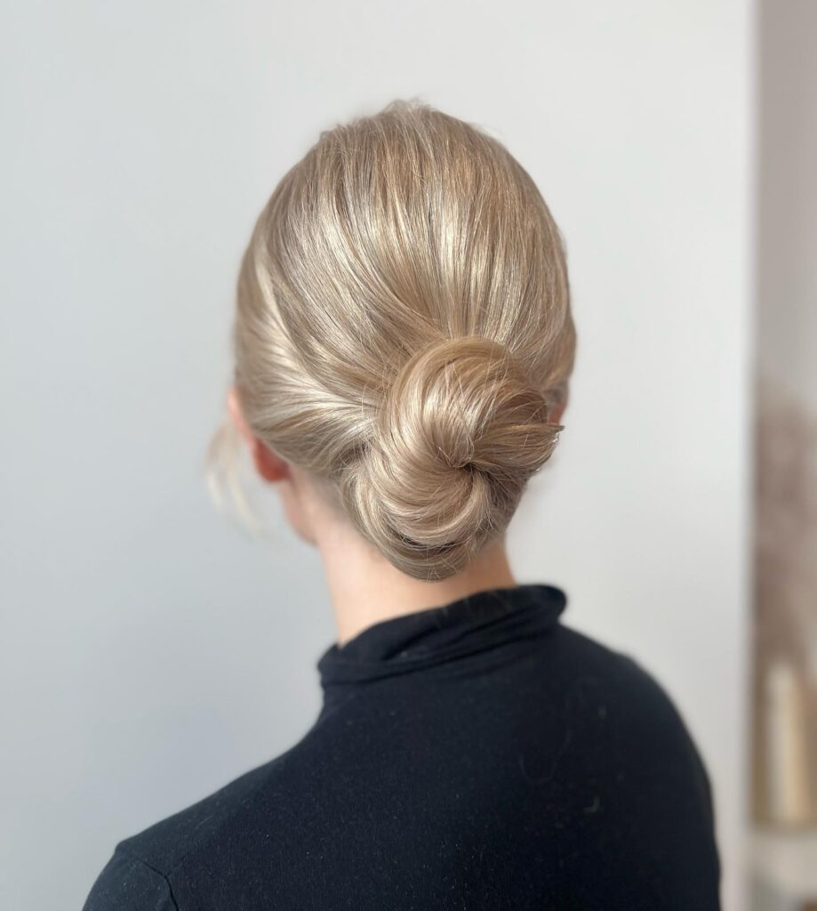 Blonde hair styled into a sleek low knot bun with a smooth and polished finish.