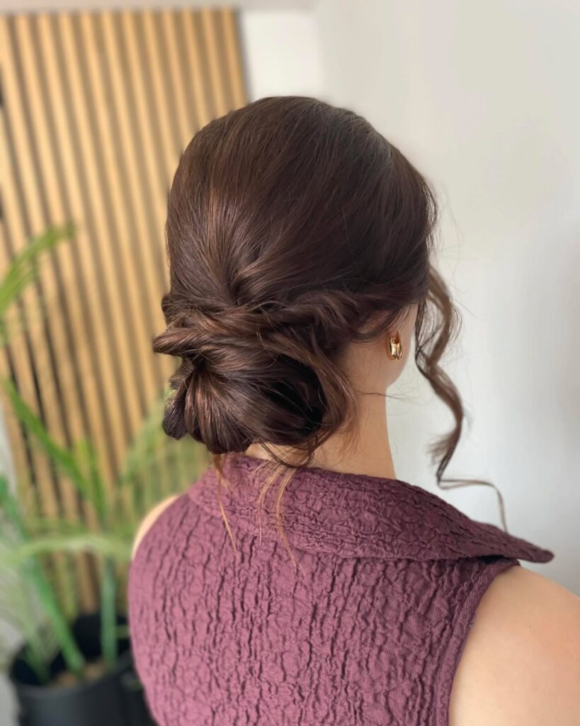 Brunette hair styled in a textured low bun with soft face framing strands.